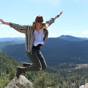 Bild zeigt leger gekleidete Frau die von einem Felsen freudig in die Höhe springt.