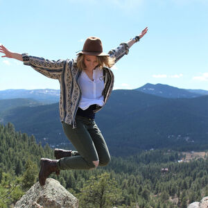 Bild zeigt leger gekleidete Frau die von einem Felsen freudig in die Höhe springt.